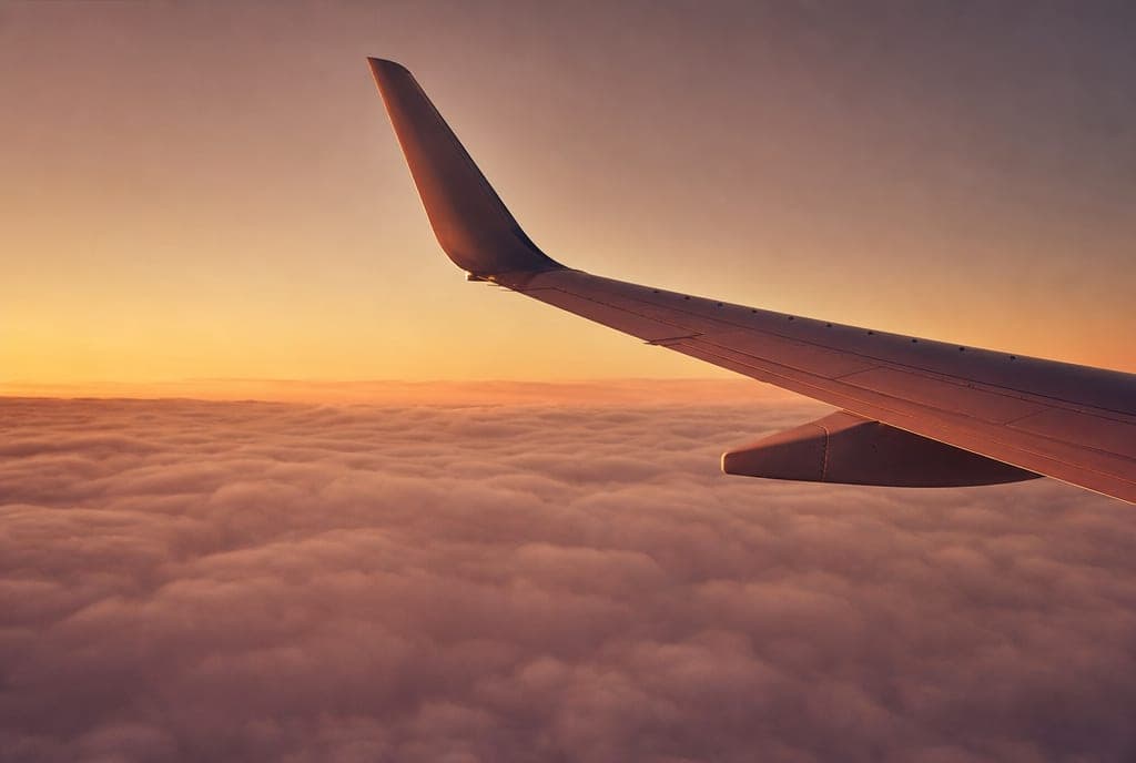 An aircraft wing tip above soft cloud at first light